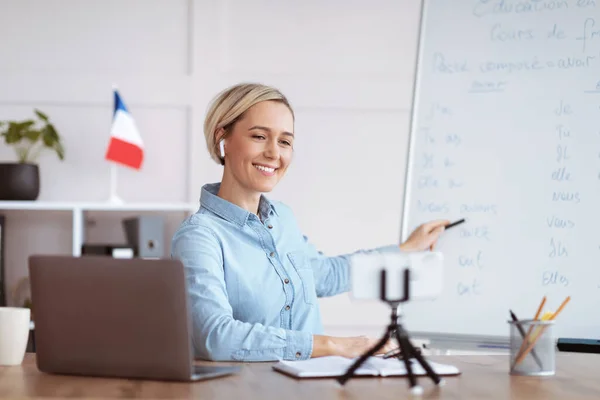 Amigável tutor do sexo feminino apontando para quadro-negro com regras de gramática francesa, conduzindo aula on-line de casa — Fotografia de Stock