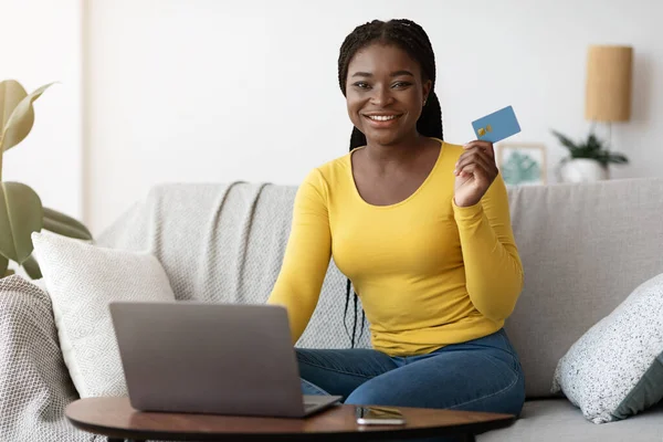 Pago en línea. Negro femenino celebración de la tarjeta de crédito y el uso de ordenador portátil en casa —  Fotos de Stock