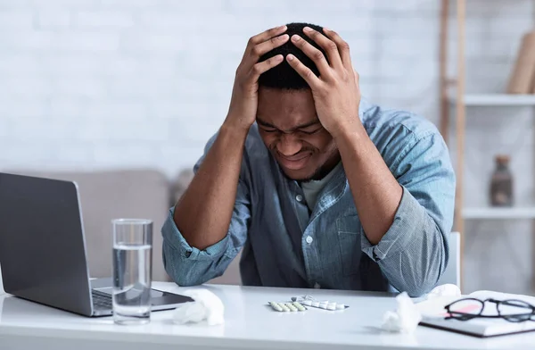 Hombre negro que sufre de dolor de cabeza tocando la cabeza sentado en el lugar de trabajo — Foto de Stock