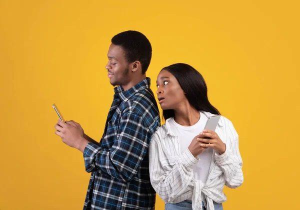 Geïnteresseerd Afrikaans Amerikaans student dame in casual kijkt in de telefoon van lachende echtgenoot — Stockfoto