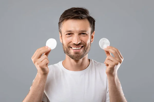 Cheerful man showing cotton pads on grey — Stock Photo, Image