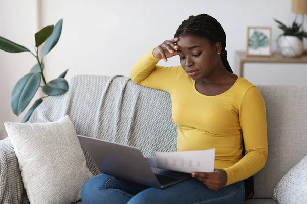 Negocio remoto. Mujer africana revisando papeles y trabajando con el portátil en casa — Foto de Stock