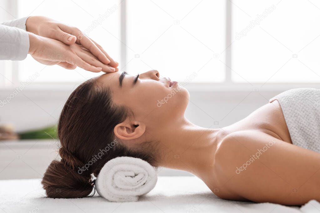 Beautiful asian woman in spa salon enjoying acupressure head massage, side view