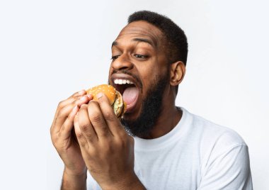 Afrikalı Adam Açgözlülükle Burger yiyor Beyaz Arkaplanda Fast food 'un tadını çıkarıyor