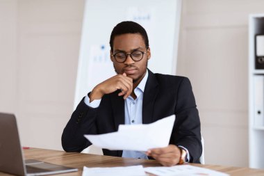 Düşünceli siyah yönetici ofiste oturuyor, gazete okuyor.