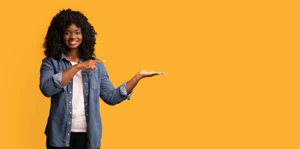 Pretty black woman pointing at copy space on yellow — Stock Photo, Image