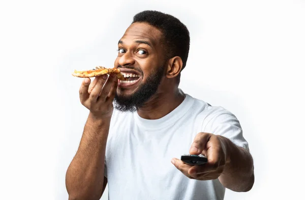 Africano cara comendo pizza e assistindo televisão em fundo branco — Fotografia de Stock