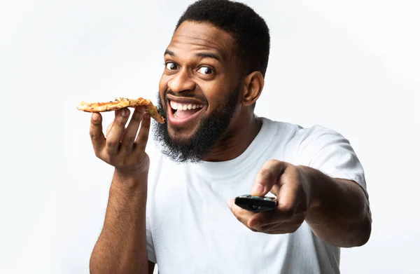 Hombre negro comiendo pizza y viendo televisión sobre fondo blanco — Foto de Stock