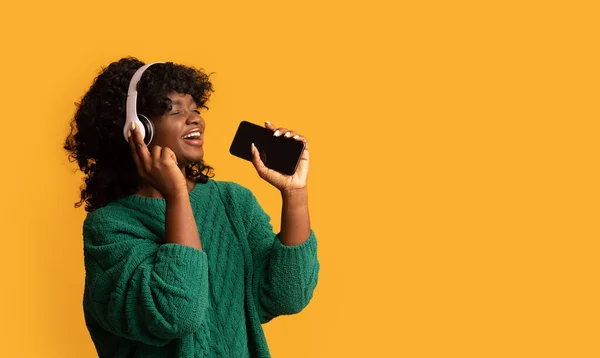 Femme noire avec smartphone et casque chantant sur jaune — Photo