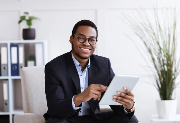 Усміхнений чорний менеджер у костюмі тримає цифровий планшет, інтер'єр офісу — стокове фото