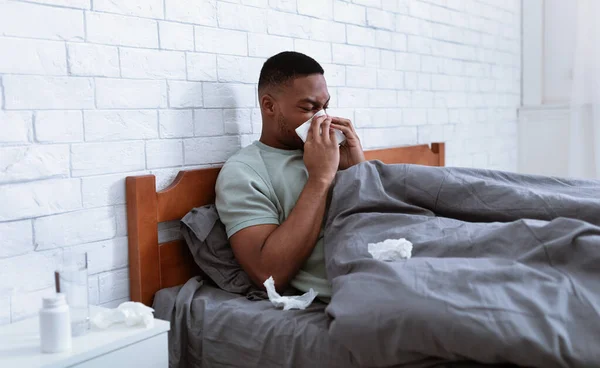 Hombre enfermo soplando la nariz en el tejido acostado en la cama interior — Foto de Stock