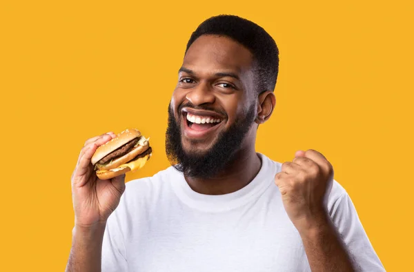 Alegre preto cara segurando hambúrguer Gesturing sim sobre amarelo fundo — Fotografia de Stock
