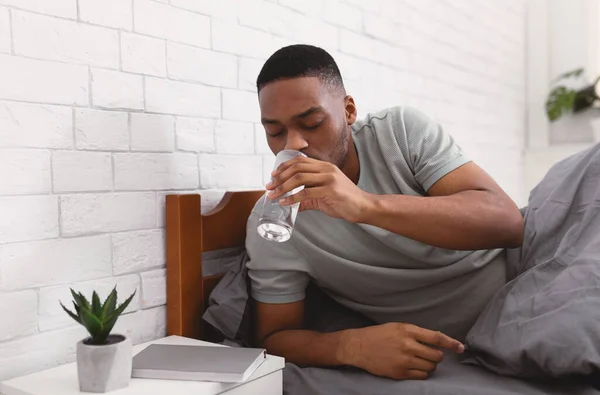 Negro hombre tomando vaso de agua en cama en mañana — Foto de Stock