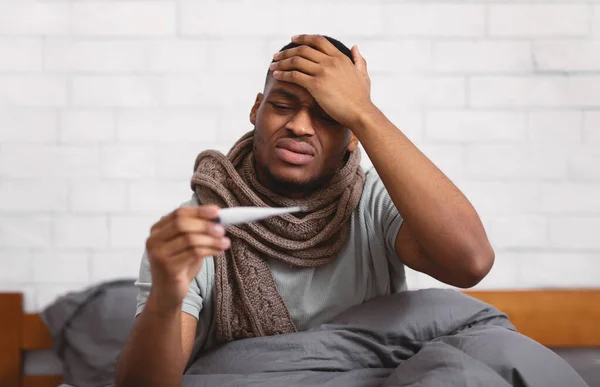 Ill African Guy Having Fever Measuring Temperature Sitting In Bedroom