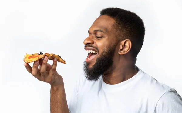 Africano cara comer fatia de pizza, fundo branco, vista lateral — Fotografia de Stock