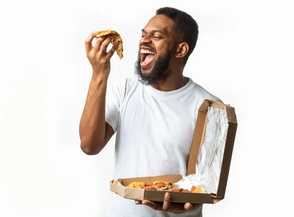 Fome preto cara comer pizza fatia de pé sobre branco fundo — Fotografia de Stock