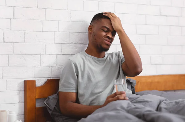 自宅でベッドに座って頭痛の種から苦しむ黒人男 — ストック写真