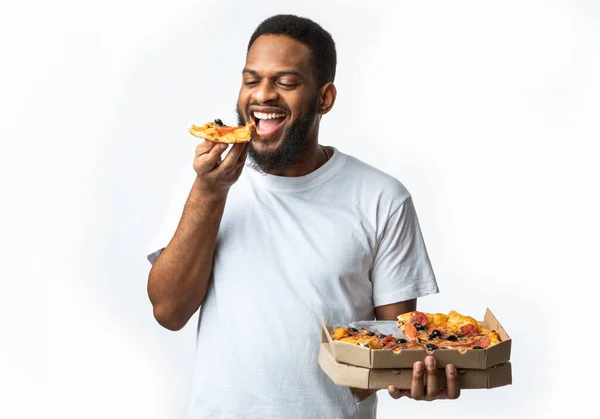Fome preto cara comer pizza segurando caixa de pé no estúdio — Fotografia de Stock
