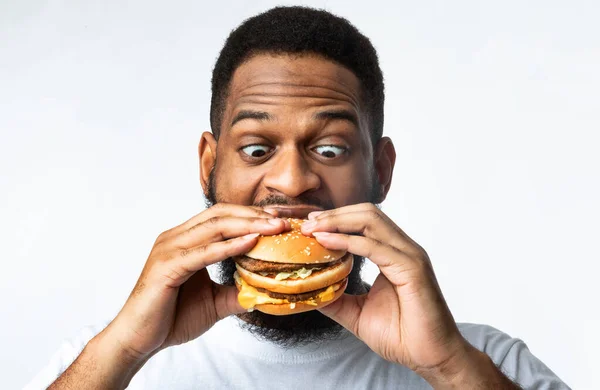 Divertido hambriento africano comiendo hamburguesa de pie sobre fondo blanco — Foto de Stock