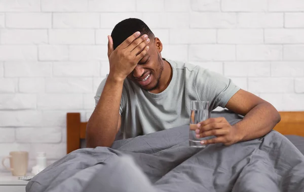 Hombre negro con dolor de cabeza sufriendo de dolor sentado en el dormitorio — Foto de Stock