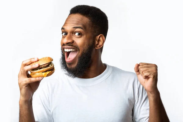 Alegre preto cara mordendo hambúrguer desfrutando fraude refeição branco fundo — Fotografia de Stock