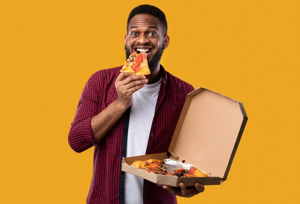 Hombre africano comiendo pizza sonriendo a cámara sobre fondo amarillo — Foto de Stock