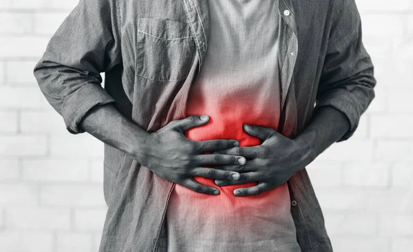 Hombre africano irreconocible con dolor de estómago tocando el abdomen en la pared gris — Foto de Stock