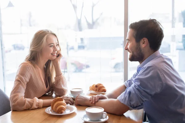 Pozytywna młoda para je razem śniadanie w kawiarni, siedzi przy oknie i cieszy się rozmową — Zdjęcie stockowe
