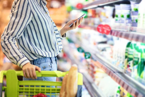 Young woman with cellphone shopping in supermarket — Stock Photo, Image