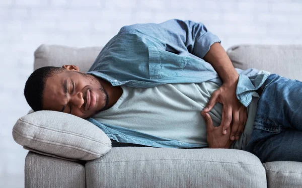 Africain gars souffrant de douleur abdominale allongé sur canapé intérieur — Photo