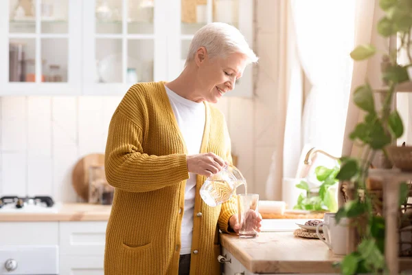 魅力的な祖母は自宅で台所に水を注ぐ — ストック写真