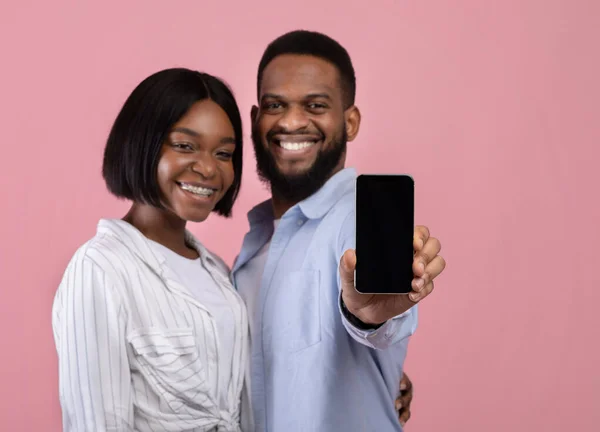 Romântico namoro aplicativo. Casal preto afetuoso mostrando telefone celular com tela vazia no fundo rosa, mockup — Fotografia de Stock