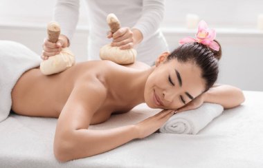 Genç Asyalı kadın vücut masajı yaptırıyor. Kaplıcada sıcak bitkisel toplarla.