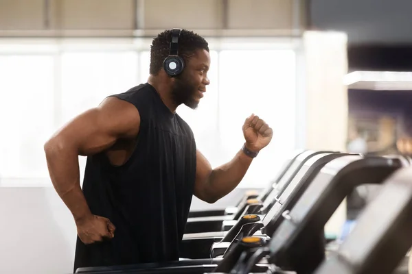 Muscular black man in modern wireless headphones running at gym — Stock Photo, Image