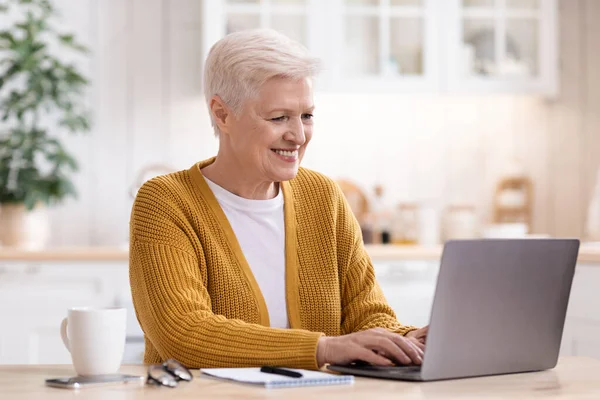 Glückliche Seniorin sitzt mit Laptop in Küche — Stockfoto