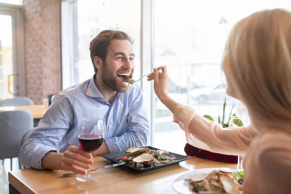 Positivo jovem casal ter romântico festivo jantar no café, comemorando aniversário, alimentando uns aos outros, beber vinho — Fotografia de Stock