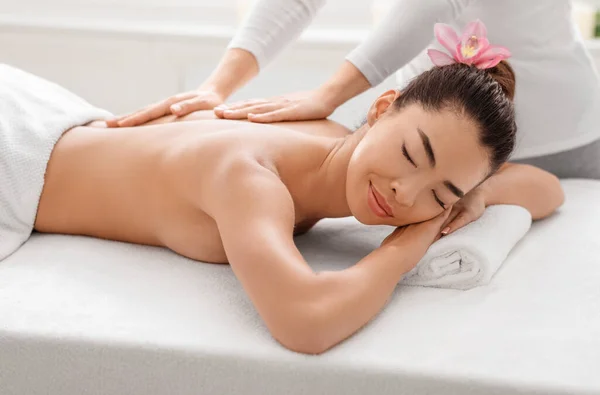A desfrutar de massagens. Linda senhora asiática relaxante durante o tratamento do corpo com massagista profissional — Fotografia de Stock