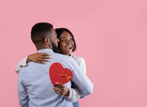 Cariñosa pareja negra con regalo de San Valentín abrazando en fondo de estudio rosa, espacio de copia — Foto de Stock