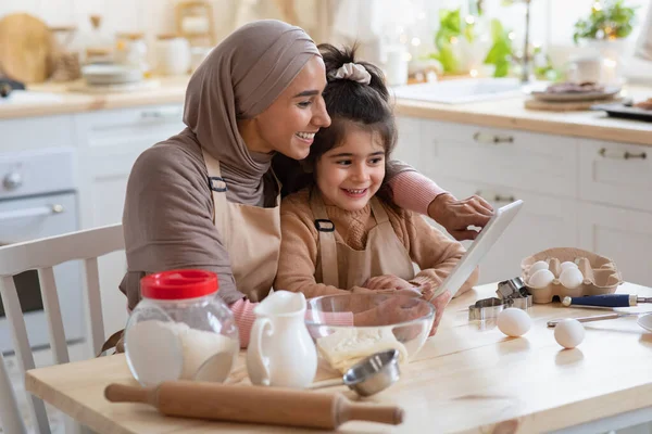 ยิ้มแม่มุสลิมและลูกสาวน้อยใช้ตารางดิจิตอลในห้องครัวด้วยกัน — ภาพถ่ายสต็อก