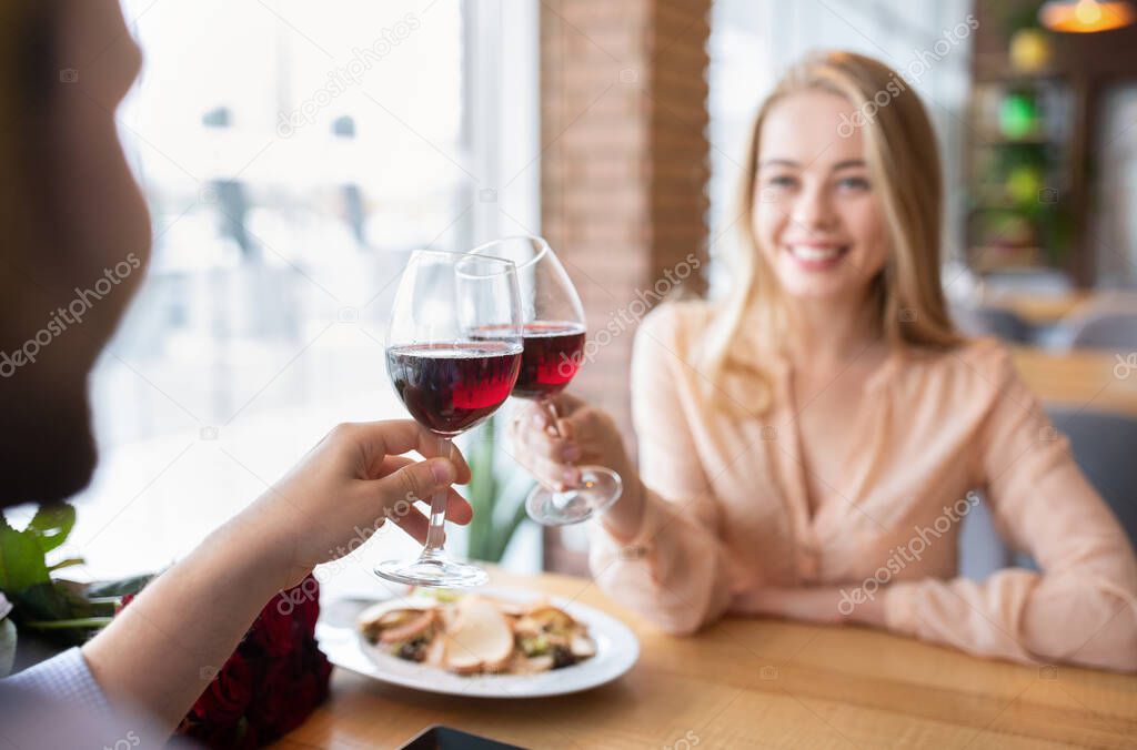 Loving millennial couple toasting red wine, saying cheers, celebrating Valentines Day in restaurant