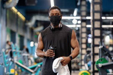 Spor salonunda egzersiz yaparken koruyucu maske takan Afrikalı kaslı adam.