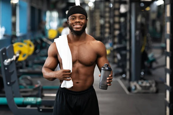 Construtor de corpo preto feliz com água e toalha no ginásio — Fotografia de Stock