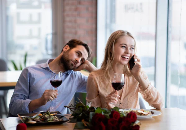 Junge Frau telefoniert bei langweiligem Date, ihr Freund fühlt sich einsam und gelangweilt im Café — Stockfoto