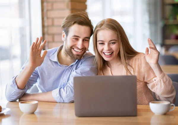 年轻夫妇在咖啡店的笔记本电脑上在线交流，一边挥手一边拍照 — 图库照片