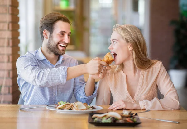 Cariñoso joven alimentando sabroso croissant a su novia en acogedora cafetería — Foto de Stock