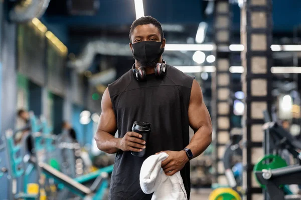 Spor salonunda egzersiz yaparken koruyucu maske takan Afrikalı kaslı adam.
