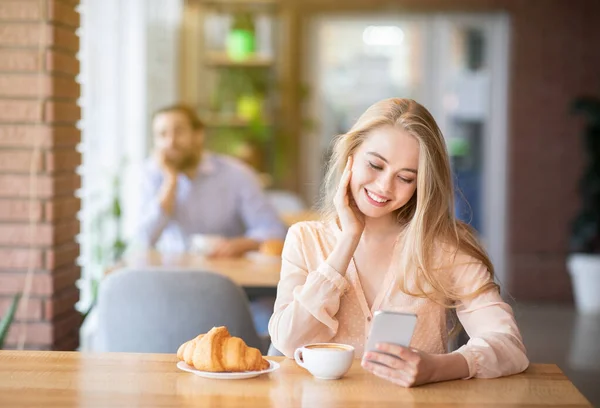 Mulher bonita usando smartphone durante o café da manhã, cara jovem olhando para ela, espaço vazio — Fotografia de Stock