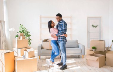 Güzel siyah kadın ve erkek arkadaşı birbirlerine bakıyorlar ve taşınma günü kutuları ile dolu bir odada kucaklaşıyorlar.