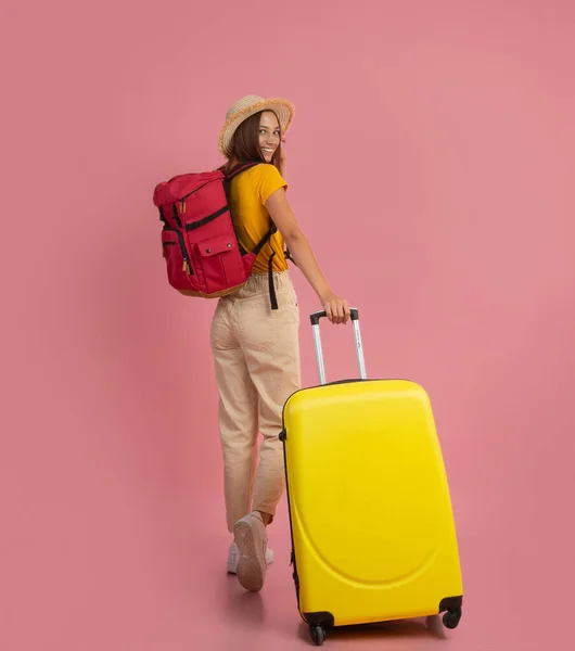 Zadní pohled na ženu batohem s kufrem na růžovém pozadí — Stock fotografie