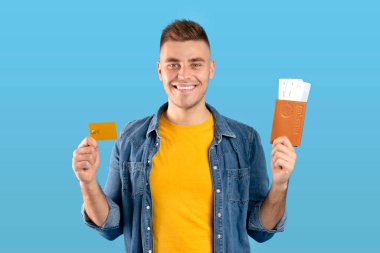 Yurtdışı seyahat bütçesi. Kredi kartı, uçak bileti ve pasaport geçmişi mavi olan genç bir adam.